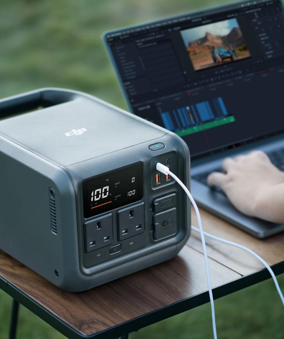 Close-up of the DJI Power 500 front panel display at 100 percent with USB-C ports and AC outlets, charging a laptop outdoors