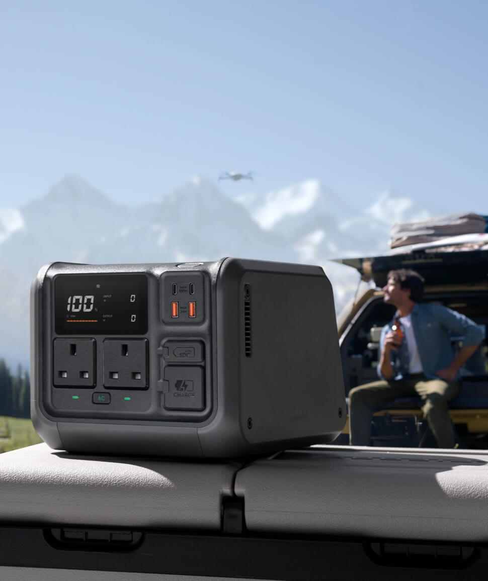 DJI Power 500 portable power station on a car in the mountains with a drone flying overhead, front display at 100 percent