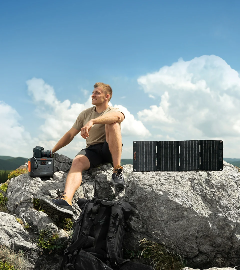 Hiker resting with the Jackery Explorer 300 Plus and a folding solar panel on a mountaintop